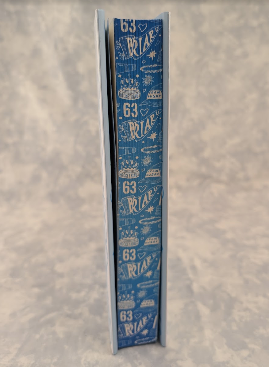 A tall, narrow book standing upright on a mottled light gray surface. The stenciled edges are covered in a repeating white pattern featuring the number 63 and small illustrated icons like cakes, stars, and bows.