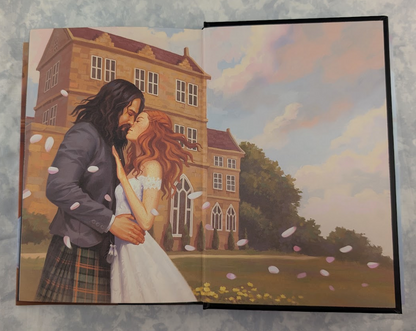 The endpapers of a hardcover book showing a romantic couple embracing in front of a large estate, photographed flat against a mottled light gray surface. The artwork depicts a man in a dark suit and plaid kilt, a woman in a white dress, falling petals, and a pastel sky.