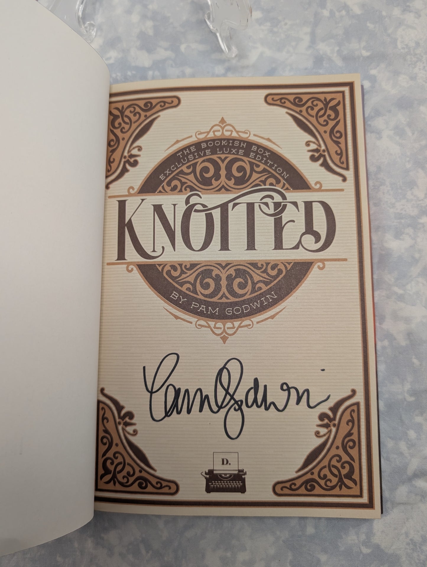 An autographed copy of the book 'Knotted' by Pam Godwin, featuring a cream-colored page with brown ornate gothic-style border designs and a black ink signature.