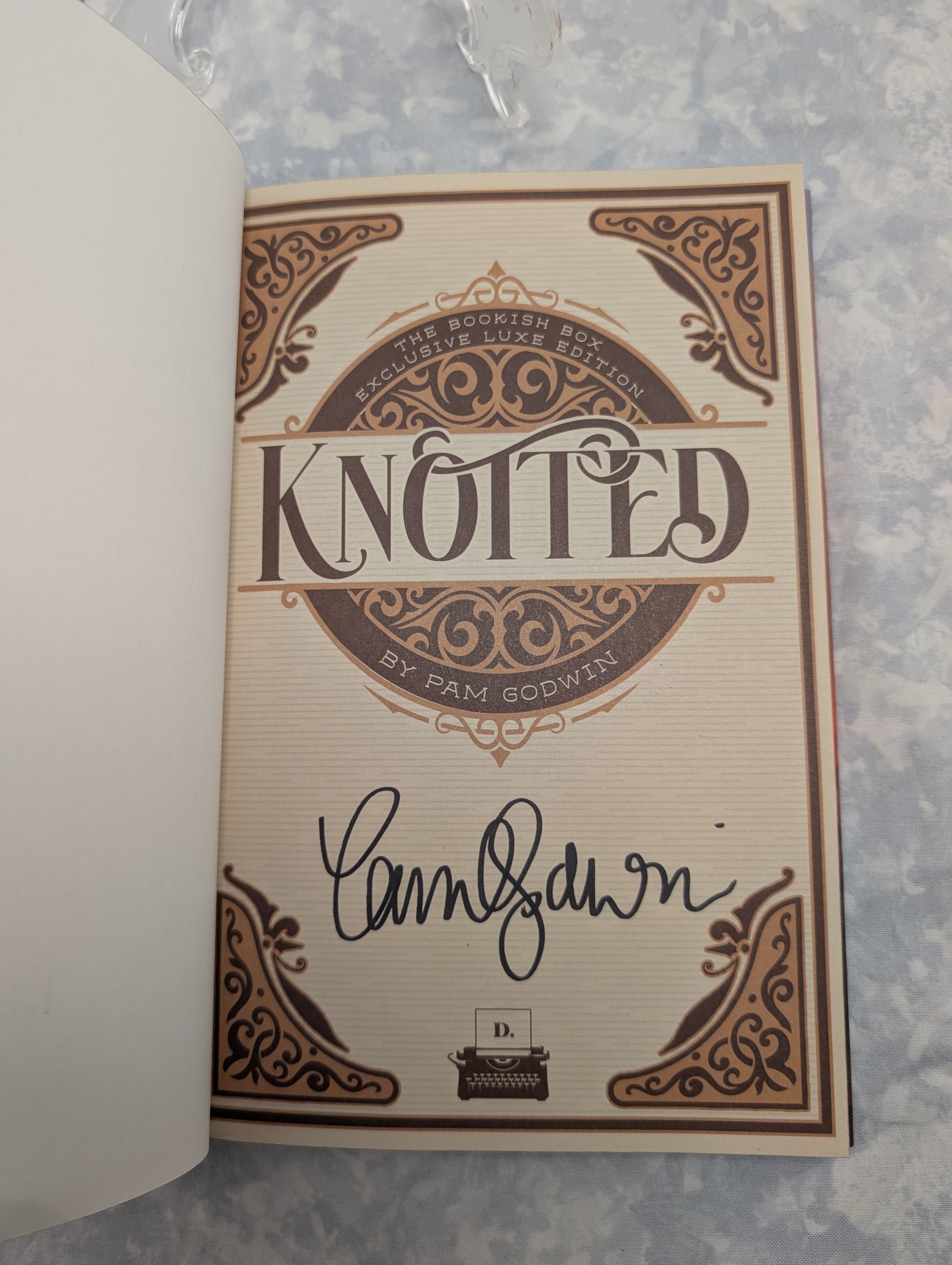 An autographed copy of the book 'Knotted' by Pam Godwin, featuring a cream-colored page with brown ornate gothic-style border designs and a black ink signature.
