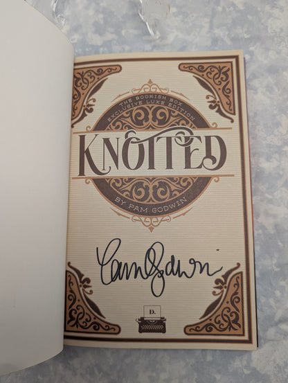 An autographed copy of the book 'Knotted' by Pam Godwin, featuring a cream-colored page with brown ornate gothic-style border designs and a black ink signature.