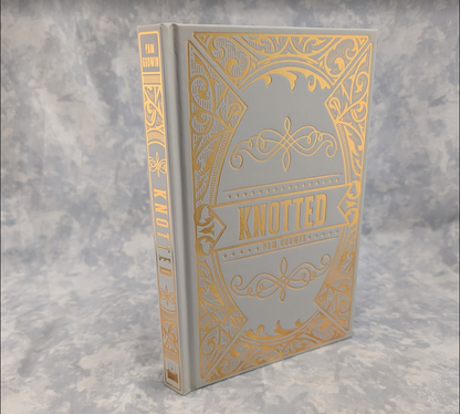 A hardcover book titled 'Knotted' featuring a light gray cover and spine with ornate gold foil detailing, set against a mottled gray background.